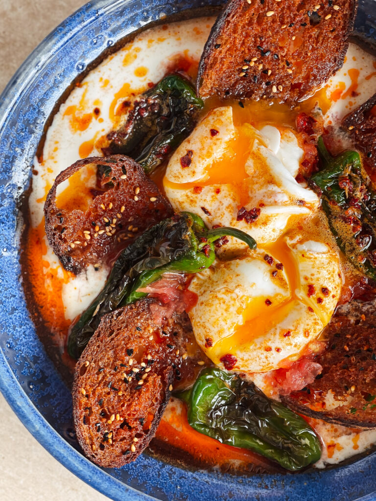 Turkish eggs or çilbir are poached eggs with garlic-y yogurt and paprika butter. We added Padron peppers, tomatoes, and deep-fried bread.